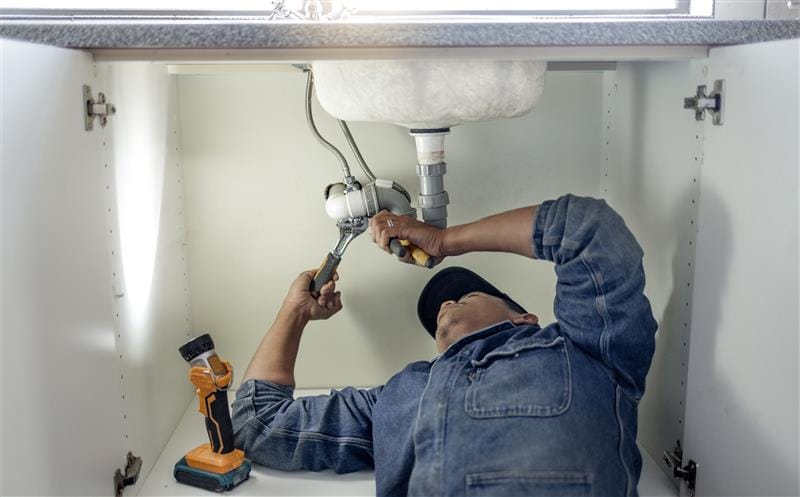Plumber repairing pipes beneath a bathroom sink in Cerritos